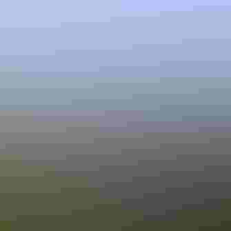 A blue sky above an expansive marsh with green marsh grass and tidal creeks